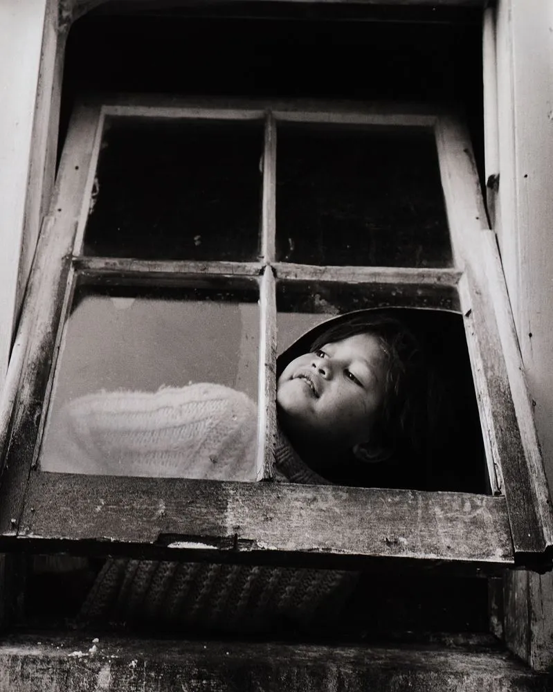 Mutu has to climb up on a box to look through the big old window at the back of the house. From the series: Washday at the pa