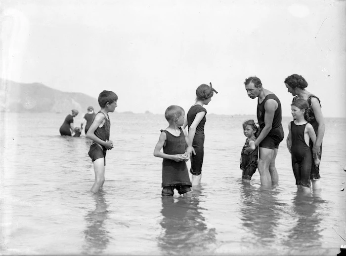 A group in bathing costumes, paddling in shallow water