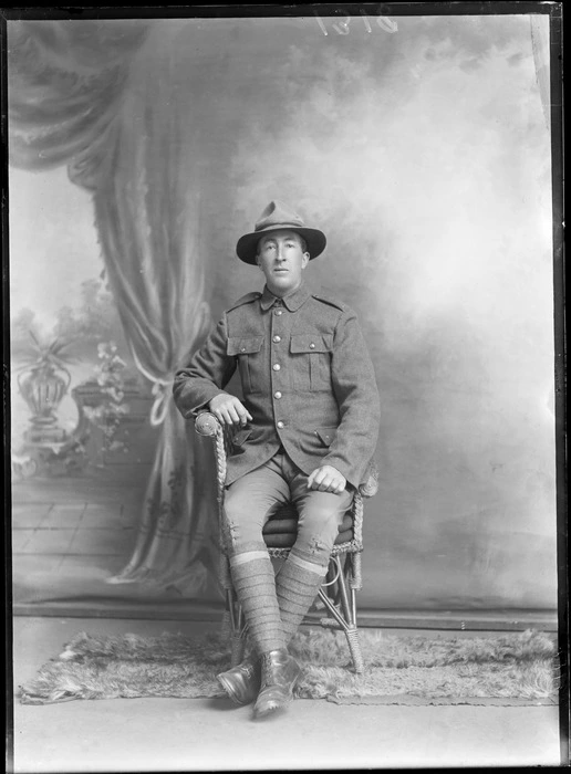 Studio portrait of an unidentified man wearing a military uniform, sitting in a chair with painted backdrop, Christchurch