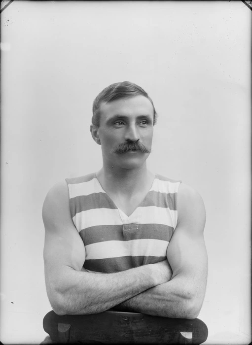 Studio upper torso portrait of an unidentified muscular man [rower, wrestler?] with large moustache in striped sleeveless sportsman's vest sitting on a chair, Christchurch