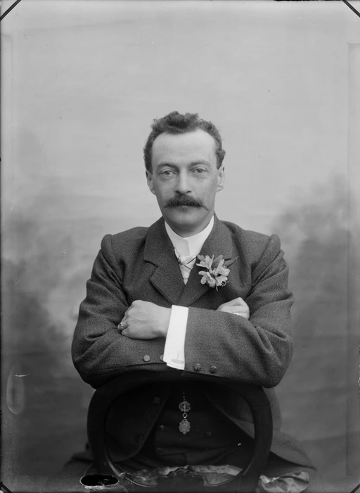 Portrait of unidentified man [groom?] with moustache sitting on wooden chair with arms folded, Christchurch