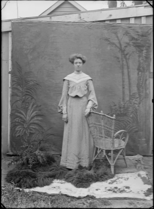 Outdoors portrait with false backdrop, unidentified woman in high neck collar dress with v-shaped shoulder design, probably Christchurch region