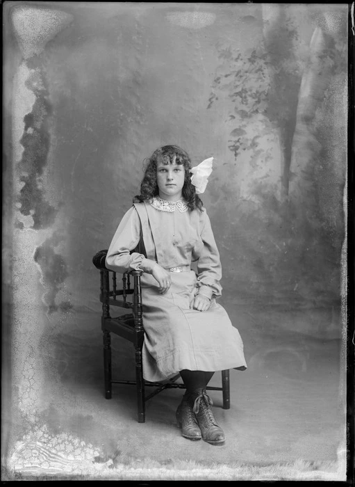 Studio portrait of unidentified girl with lace collar and hair bow sitting in wooden chair, Christchurch