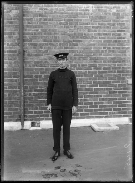 An unidentified member of the Christchurch Fire Brigade, wearing a woolen jersey with the letters 'CFB' embroidered on front, and a peaked cap with insignia, possibly Christchurch district