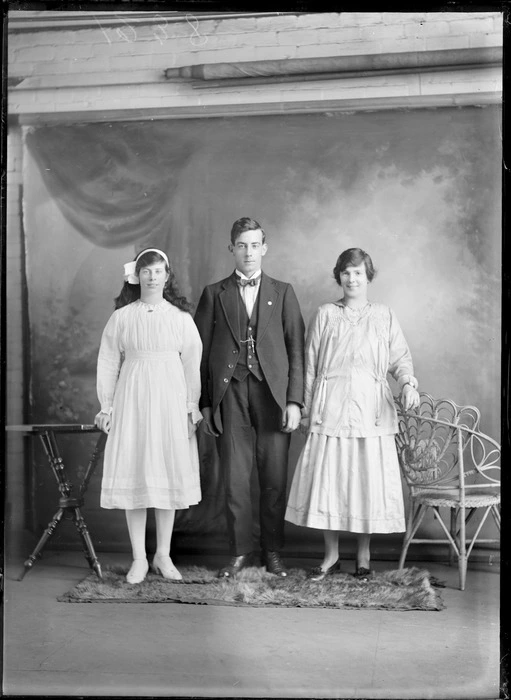 Portrait of two unidentified young women and a man, with a painted studio backdrop, probably Christchurch district