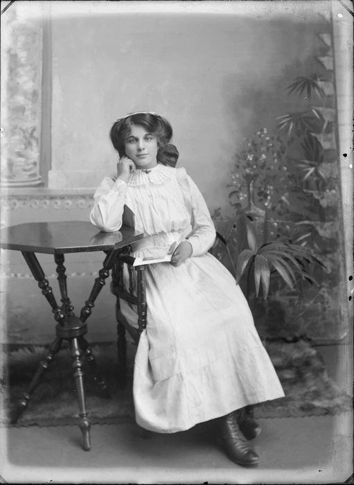 Studio unidentified portrait of a young woman with pleated collar and dress, sitting at a cane table reading a book, Christchurch