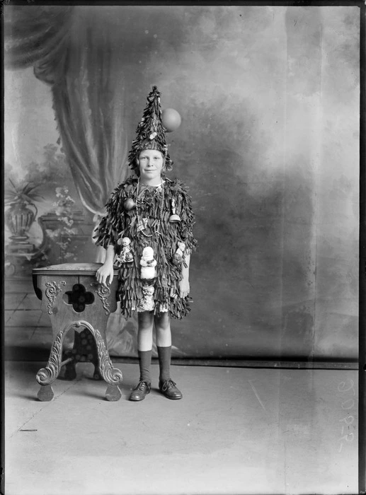 Studio portrait of unidentified girl dressed as Christmas tree with ornaments, probably Christchurch