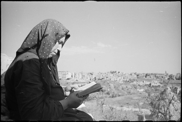 Italian peasant woman reading a bible with the ruins of Orsogna in background, Italy, World War II - Photograph taken by George Kaye
