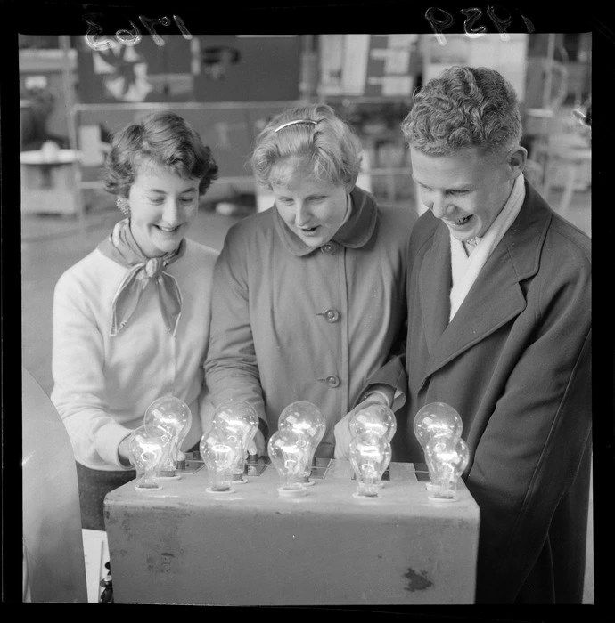 Group of unidentified young people, looking at an object with lightbulbs on it [at a science fair?]
