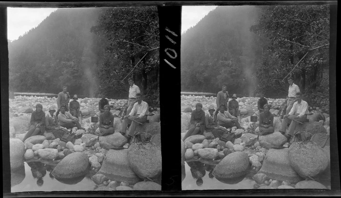 Group of men and women sitting beside a small campfire on a rocky river bed, including Edgar and Alice Williams (at the back), unknown location