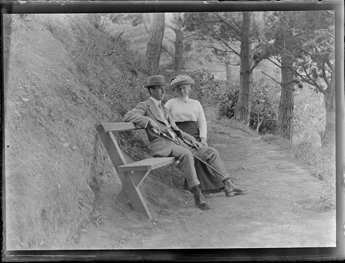 Lydia Williams with son [Owen?] on a seat and path under pine trees, [Botanic Gardens, Wellington City?]