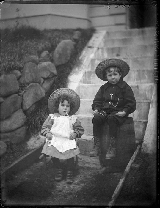 Owen sitting on small chair with pipe in his mouth and Edgar sitting on a barrel, at the Williams' home, Kew, Dunedin