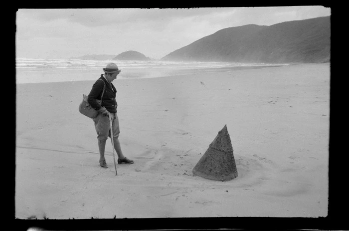 Alice Williams viewing a metal coned object on the beach, including hills in the background, Mason Bay, Stewart Island (Rakiura)