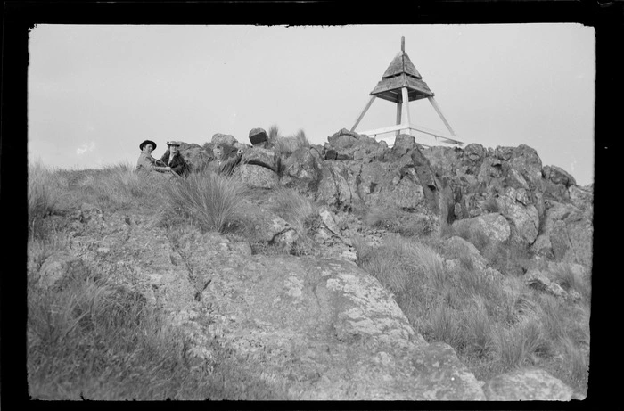 Group, including Edgar Williams on right, sitting on rocky hillside beneath trig station, [Port Hills, Canterbury region?]