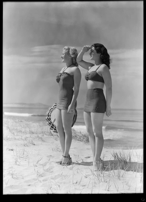 Two women model their bathing suits at the beach