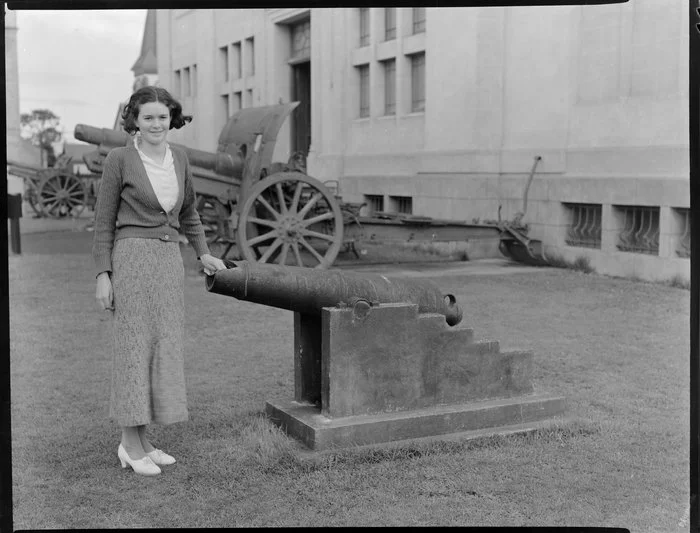 Unidentified young woman standing beside military cannon [outside a museum? Christchurch?]