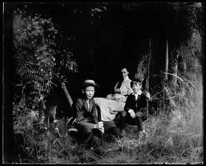 Two boys and a woman seated among trees