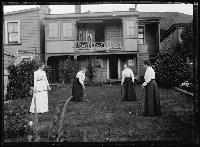 Four women playing croquet in the backyard of a house