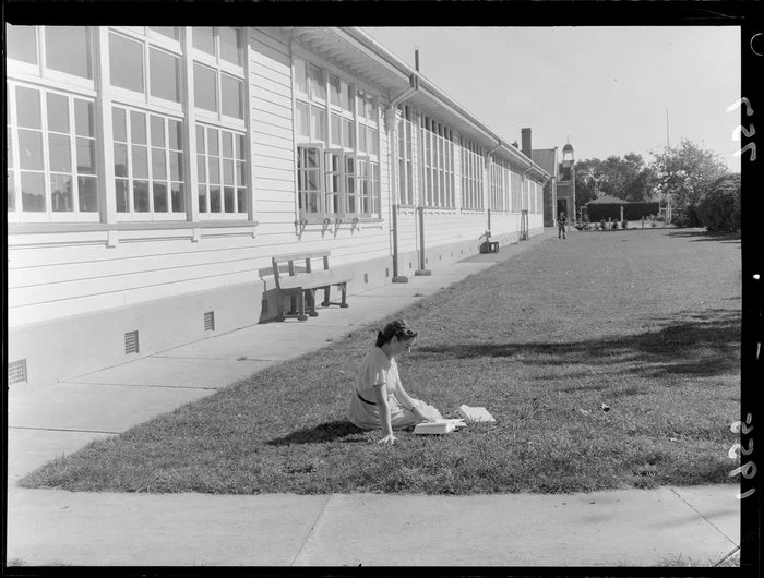 Young girl, reading on the grass in front of a school, during a water shortage, Marton, Rangitikei District