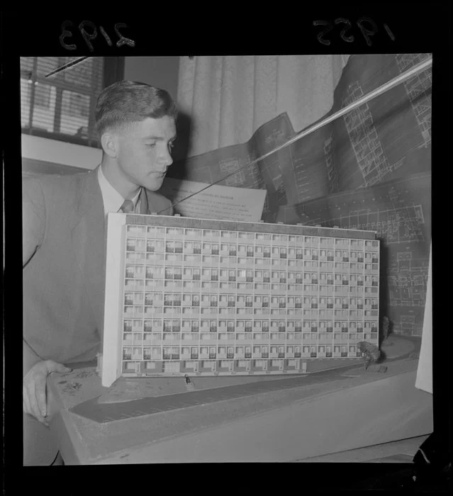 Man with an architectural model of a prototype high-rise State Advances Corporation housing block, at housing exhibition, Drapery and General Importing Company of New Zealand Ltd gallery