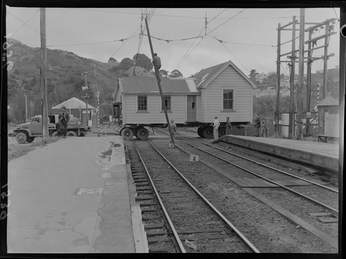 A house, which is being relocated, is towed over the railway tracks, including a man on a ladder