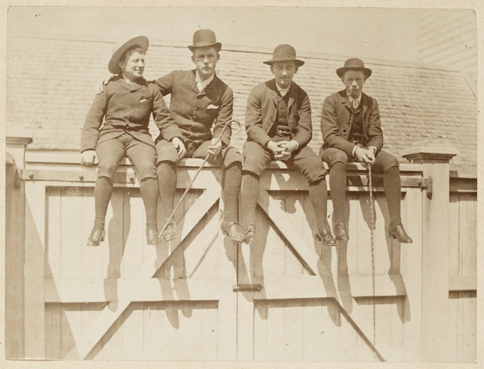 Four men sitting on top of a gate