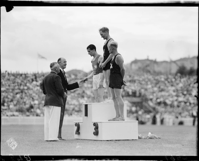 Winning athletes on podium during awards ceremony for the six mile event, 1950 British Empire Games, Eden Park, Auckland