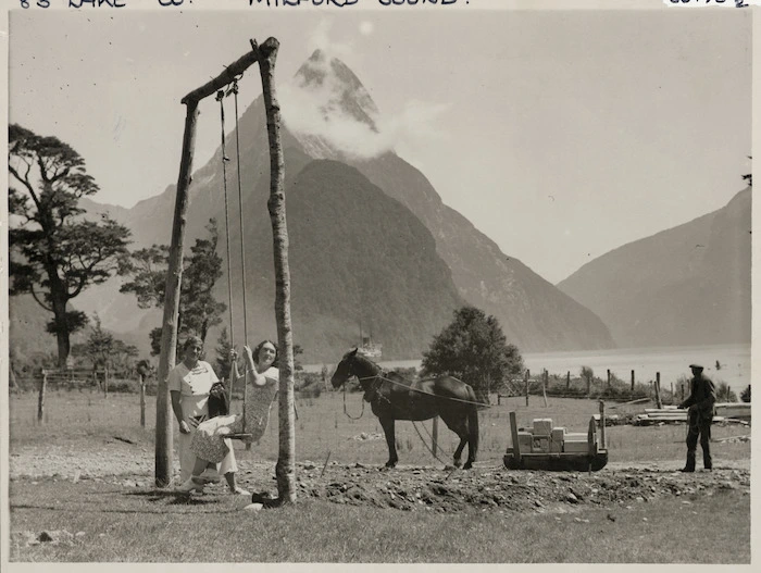 Two unidentified women on a swing, and a man unloading stores, Milford Sound