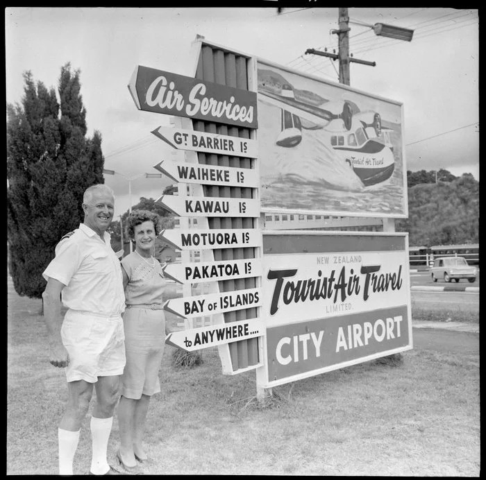 Fred and Mabel Ladd with Tourist Air Travel sign, Auckland Airport