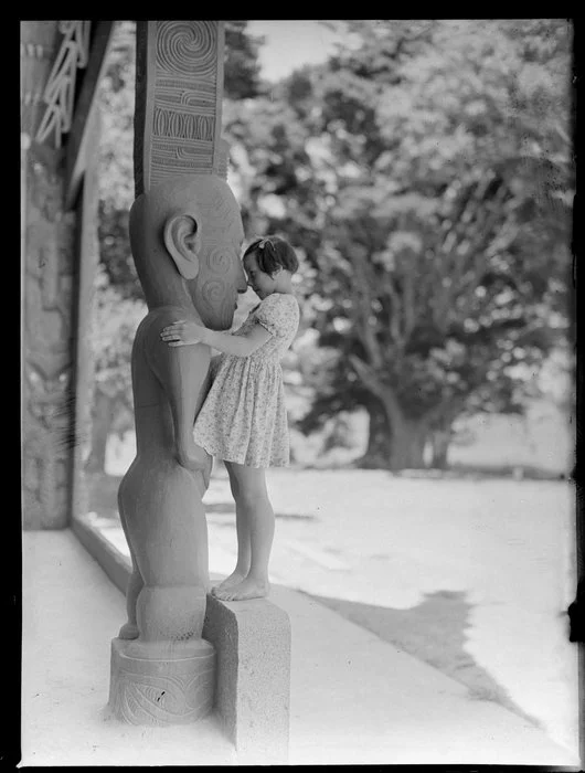 Summer Child Studies series, unidentified young girl, rubbing noses with a carved Maori post