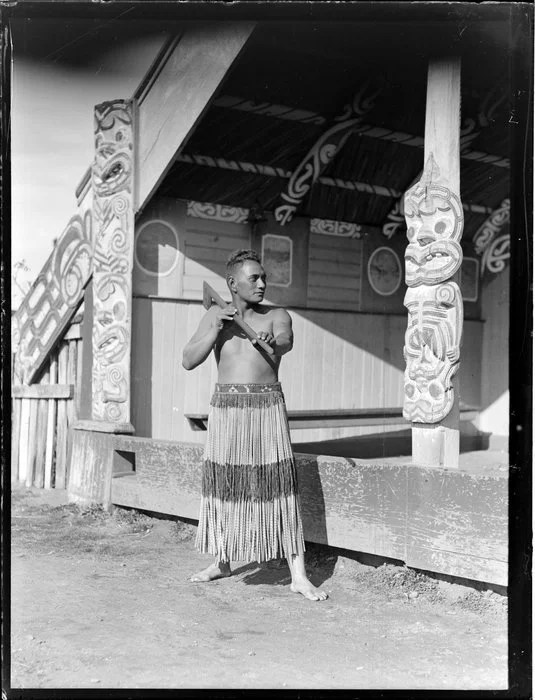 Portrait of Ninihi (Jack) Kuru holding a tewhatewha outside the wharenui at Otukou marae, Lake Rotoaira