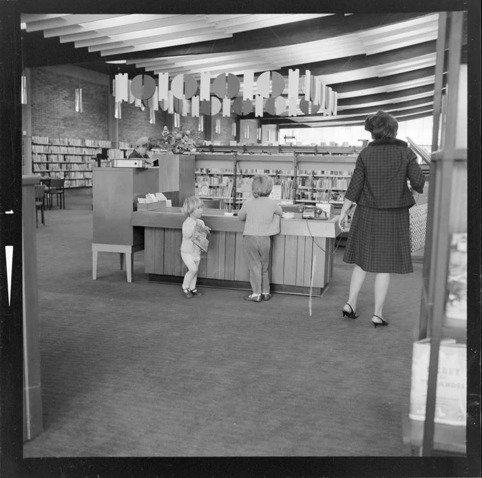 Two children and woman at counter, Gisborne Public Library