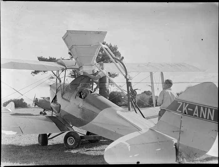 Farmland at Ihumatao, Mangere, Manukau city, Auckland Region, featuring fertiliser being funnelled into an aerial topdressing plane [ZK-ANN Tiger Moth?] by unidentified men