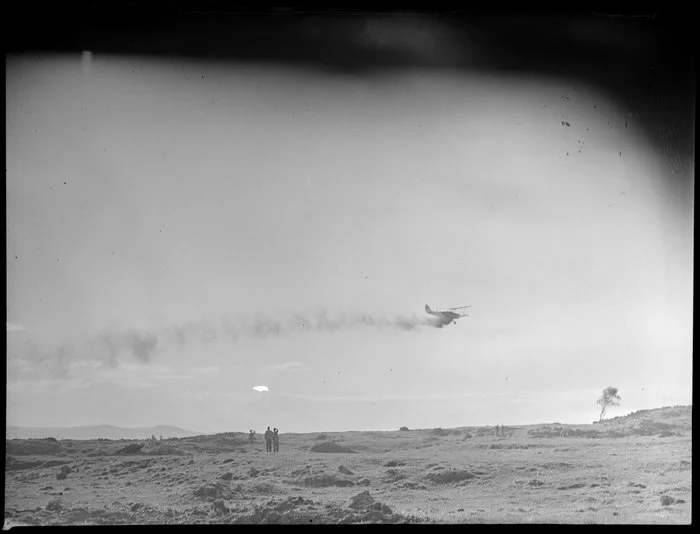 Farmland at Ihumatao, Mangere, Manukau City, Auckland Region, featuring an aerial topdressing plane [ZK-ANN Tiger Moth?] in action, with onlookers standing in the paddock