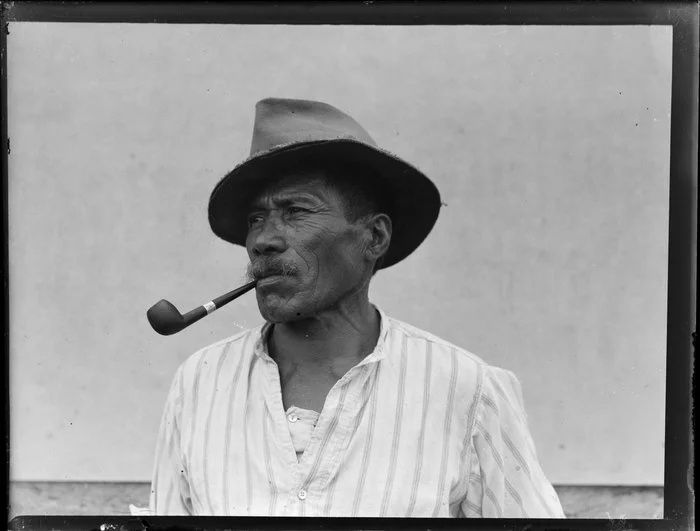 Portrait of Ripo Warena smoking pipe and wearing a hat, location unknown