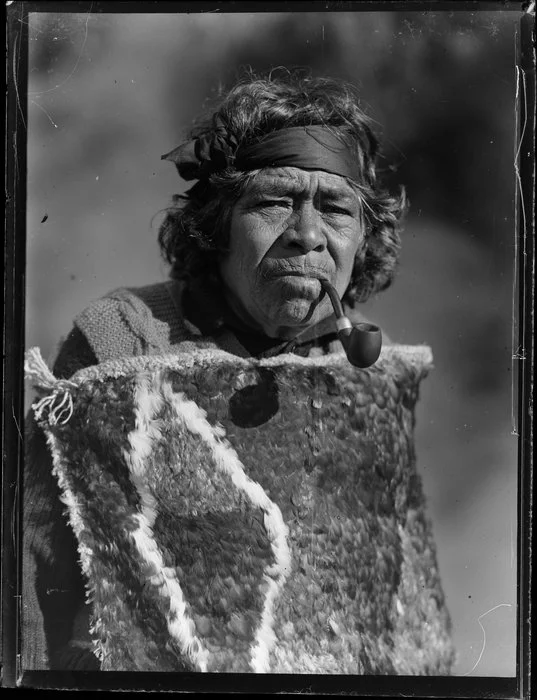 Portrait of Maori kuia Marutuna of Orakei Korako smoking a pipe and wearing a traditional feather cloak