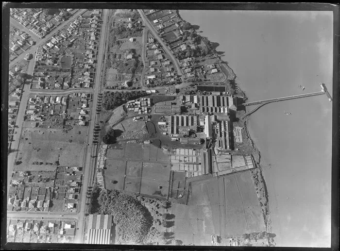 Close-up view over the New Zealand Refrigerating Company, Imlay Freezing Works Imlay Place, Wanganui, with stock pens and yards, and effluent treatment ponds, and stacks of timber next to residential housing with Heads Road, Balgownie Avenue and Wordsworth Street, located beside the Wanganui River with wharf for loading ships