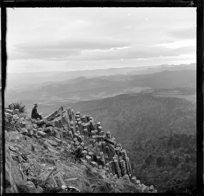 Man seated on a rocky precipice looking at the view from Mount Cargill, Waikouaiti County