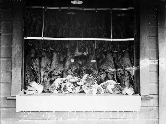Cuts of meat and carcasses in the window of E M Gibson's butcher shop