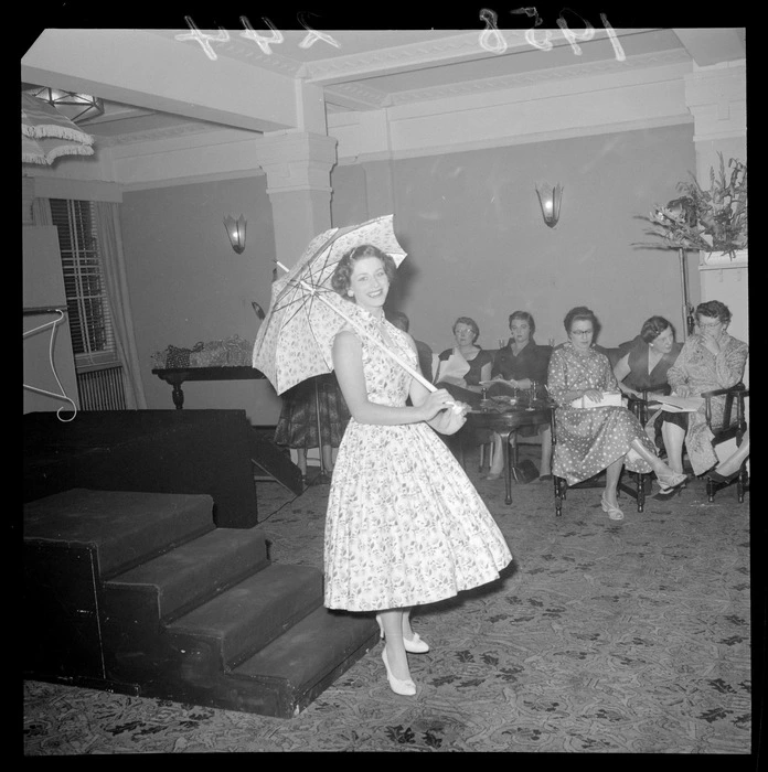 Unidentified young woman, holding a sun umbrella and wearing a summer dress, [a model at a fashion parade? Wellington?]