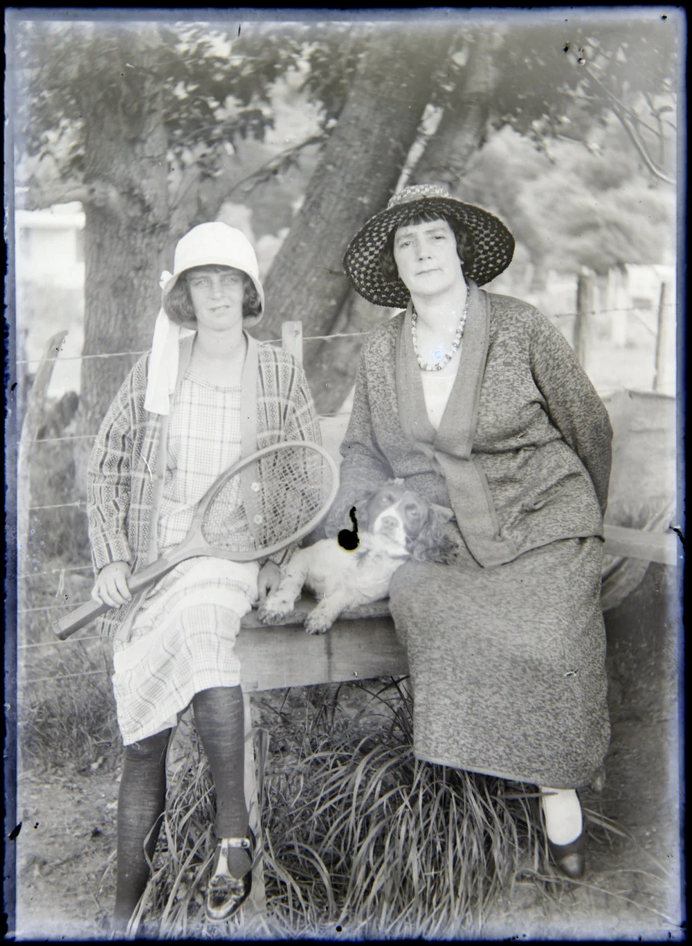 Two women seated on bench with tennis racquet